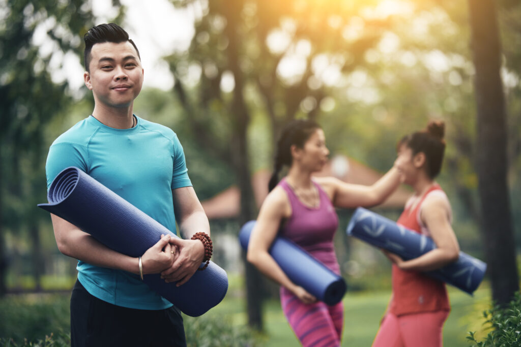 Group of fitness enthusiasts smiling and holding mats before a group workout in a nature park.